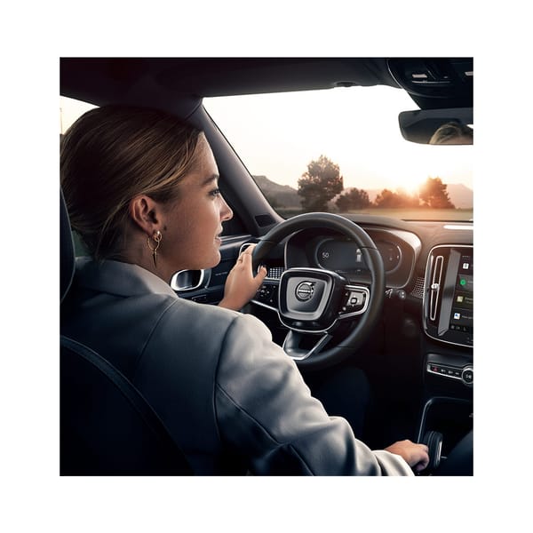 blond kvinna med uppsatt hår kör en volvo bil i solnedgången