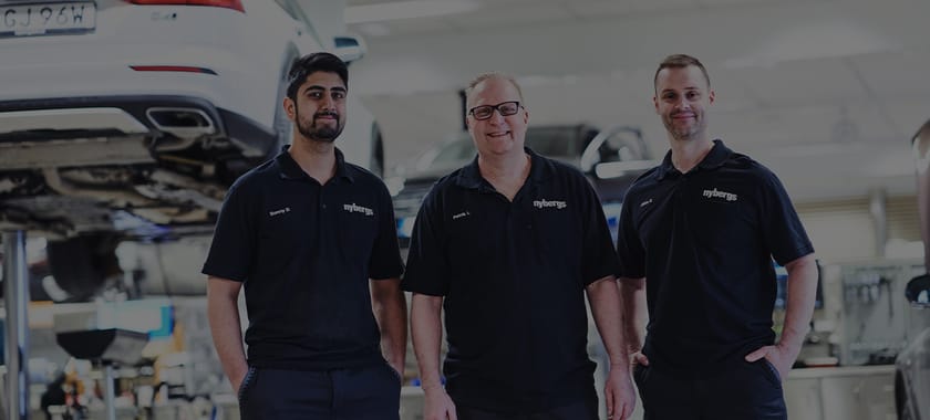 Tre mekaniker hos Nybergs Bils bilverkstad som står och ler framför en bil