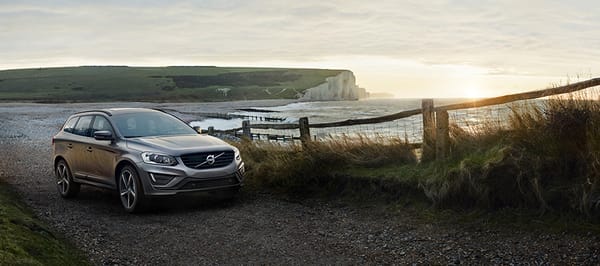 Silvrig volvobil som står på en grusväg vid vattnet med utsikt över havet och en klippvägg