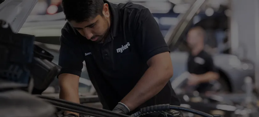 Man som reparerar något i motorhuven på en bil hos en bilservice