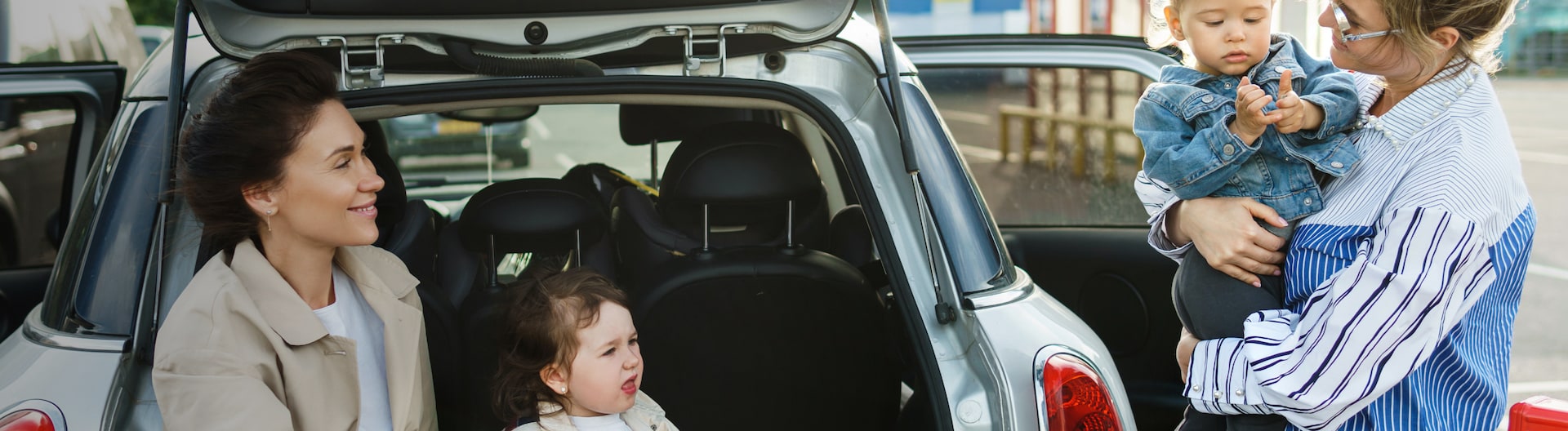 Två vuxna och två barn konverserar vid en bils bagageutrymme